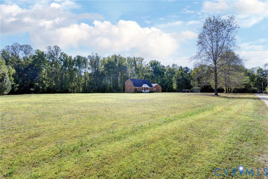 Expansive acreage featuring open green space, mature tree lines, and a brick exterior residence