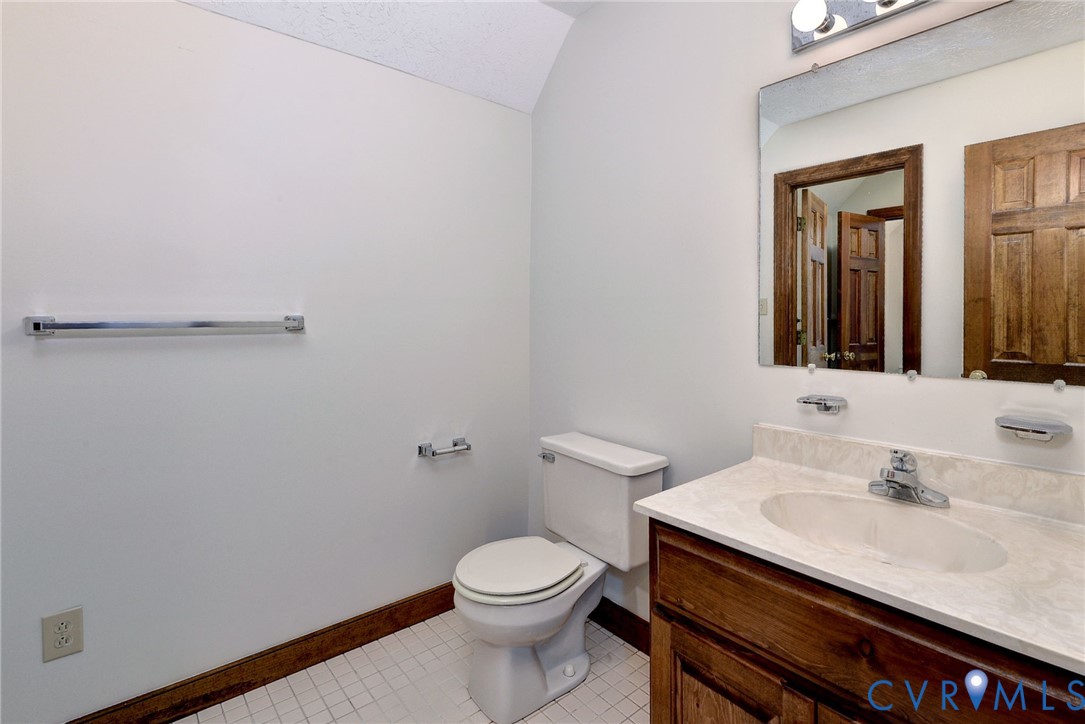 Bathroom featuring a wood-finish vanity with a stone-composite countertop, integrated sink, wall-mounted mirror, and tile flooring