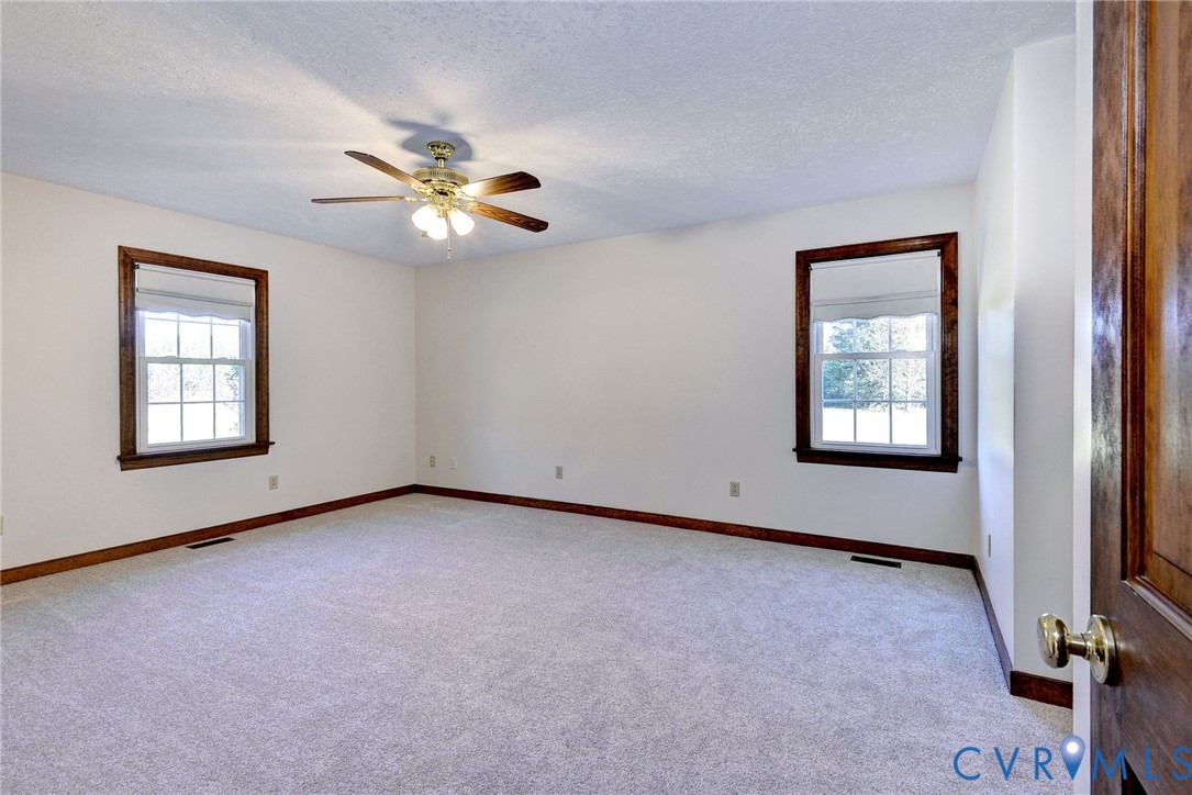 Neutral-toned carpeting, dual windows with wood-finish trim, and a multi-blade ceiling fan with integrated light fixture