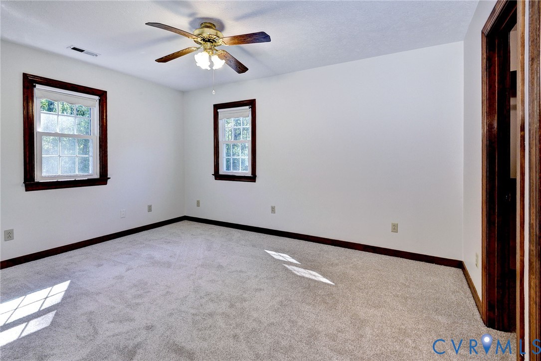Room featuring neutral carpeting, dark wood-finish window trim, and a ceiling fan with integrated light fixture