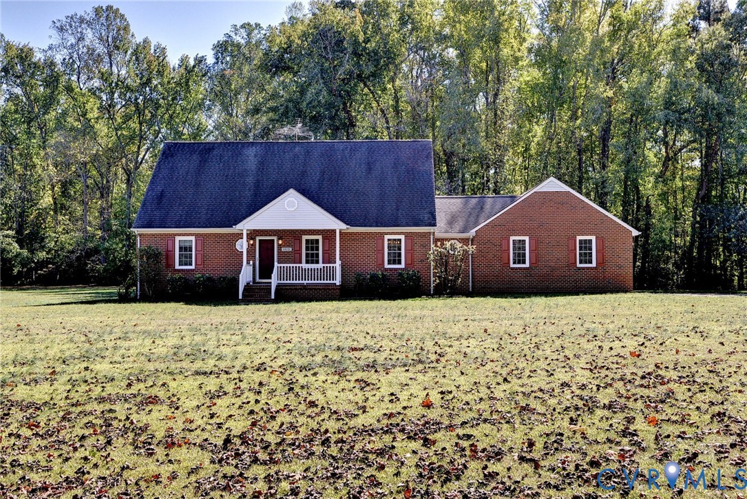 Traditional brick exterior featuring a covered front porch, gabled roofline, decorative window shutters, and expansive grounds surrounded by mature trees Traditional brick exterior featuring a covered front porch, gabled roofline, decorative window shutters, and expansive grounds surrounded by mature trees