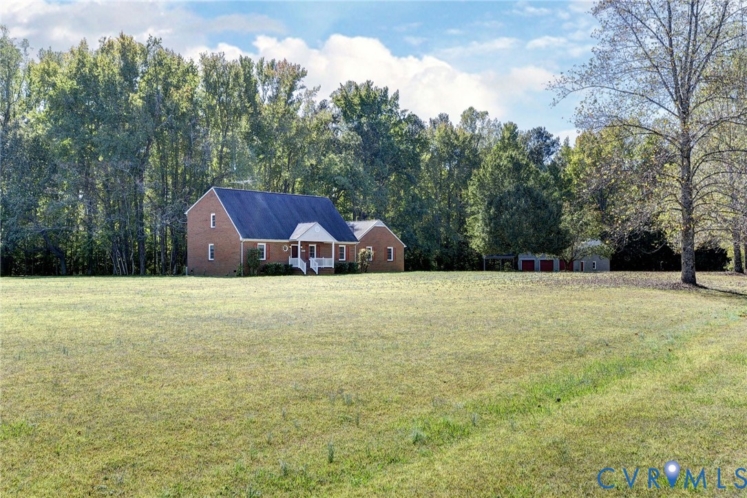 Multi-story brick exterior residence featuring a covered entryway, steeply pitched roof, expansive open lawn, and detached garage structure set against a backdrop of mature trees