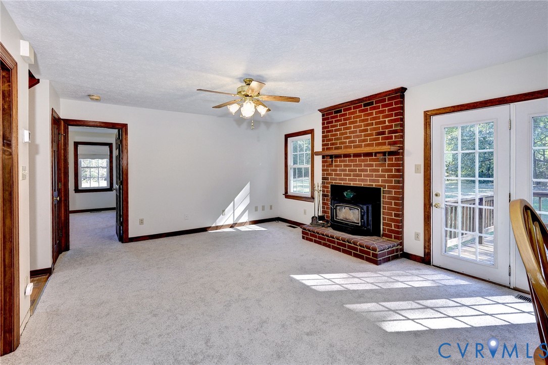 Floor-to-ceiling red brick fireplace with a wood mantle and insert, neutral wall-to-wall carpeting, ceiling fan with light fixture, and double glass-paned doors