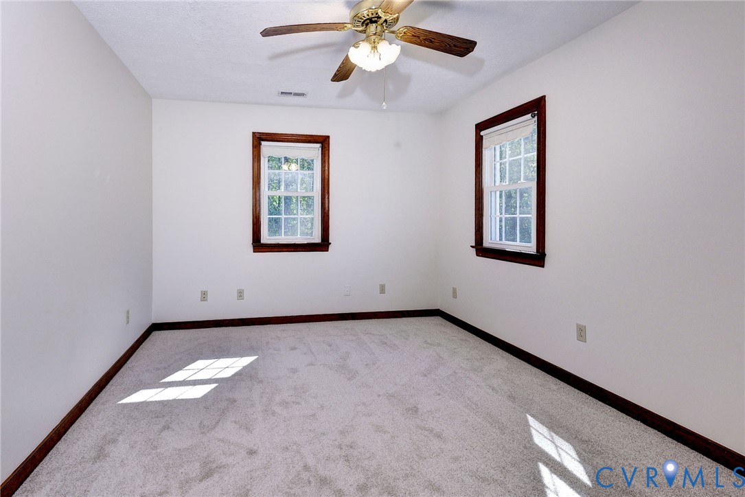 Neutral-toned interior room featuring wall-to-wall carpeting, two double-hung windows with dark wood-finish trim, and a ceiling fan with integrated lighting
