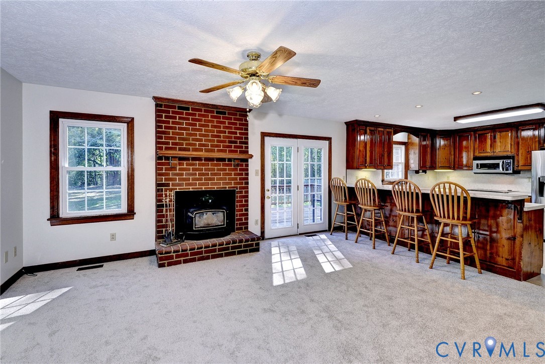 Red brick fireplace with a wood-finish mantel and inset stove, wood cabinetry, glass-paneled double doors, and a ceiling fan with integrated lighting