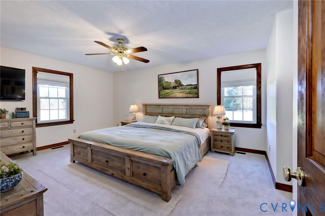 VIRTUAL STAGING - Neutral-toned room featuring double-pane windows with dark wood trim, a ceiling fan with integrated lighting, and a six-panel wood door with brass-finish hardware