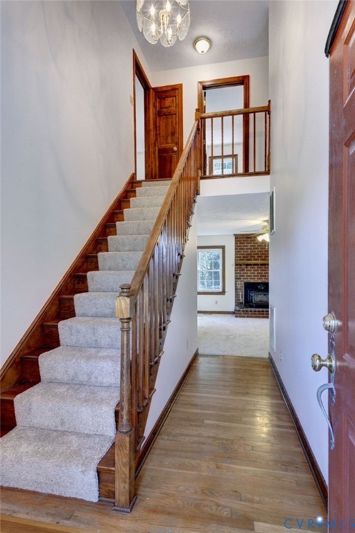 Entryway featuring wood-finish flooring, a staircase with wood railings and carpeted treads, a multi-light flush-mount fixture, and a brick fireplace