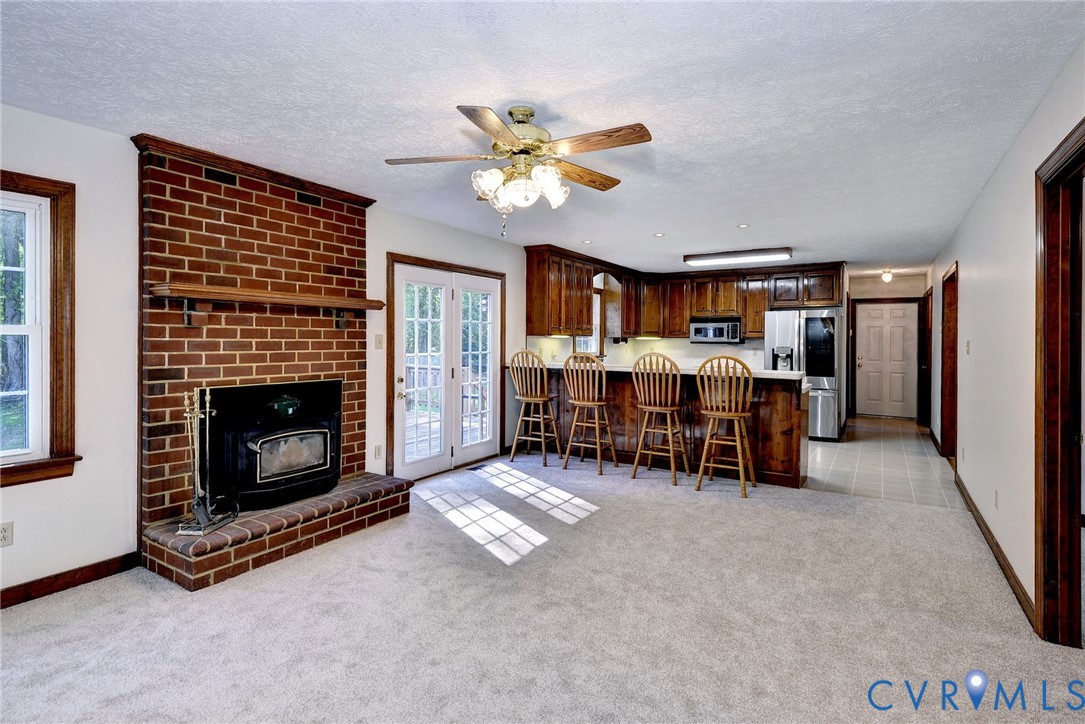 Floor-to-ceiling brick fireplace with a wood-finish mantel and inset stove, wood cabinetry, breakfast bar, and glass-paned double doors