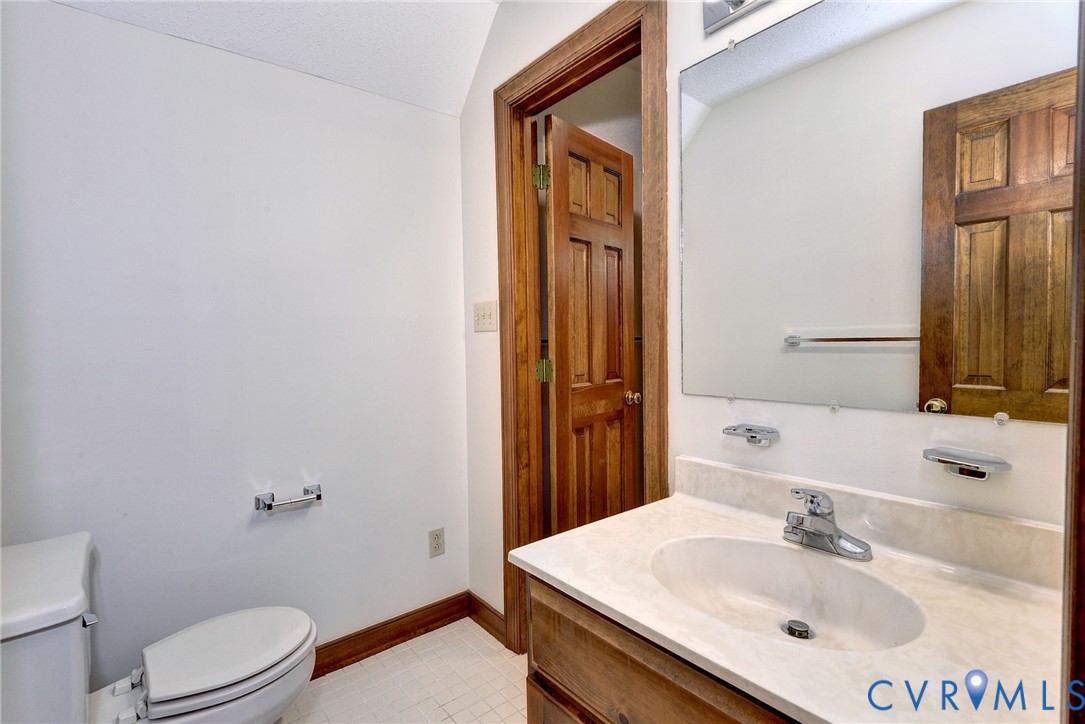 Vanity featuring a light-toned countertop with an integrated basin, wood-finish cabinetry, a large wall-mounted mirror, ceramic tile flooring, and solid wood interior door with matching trim