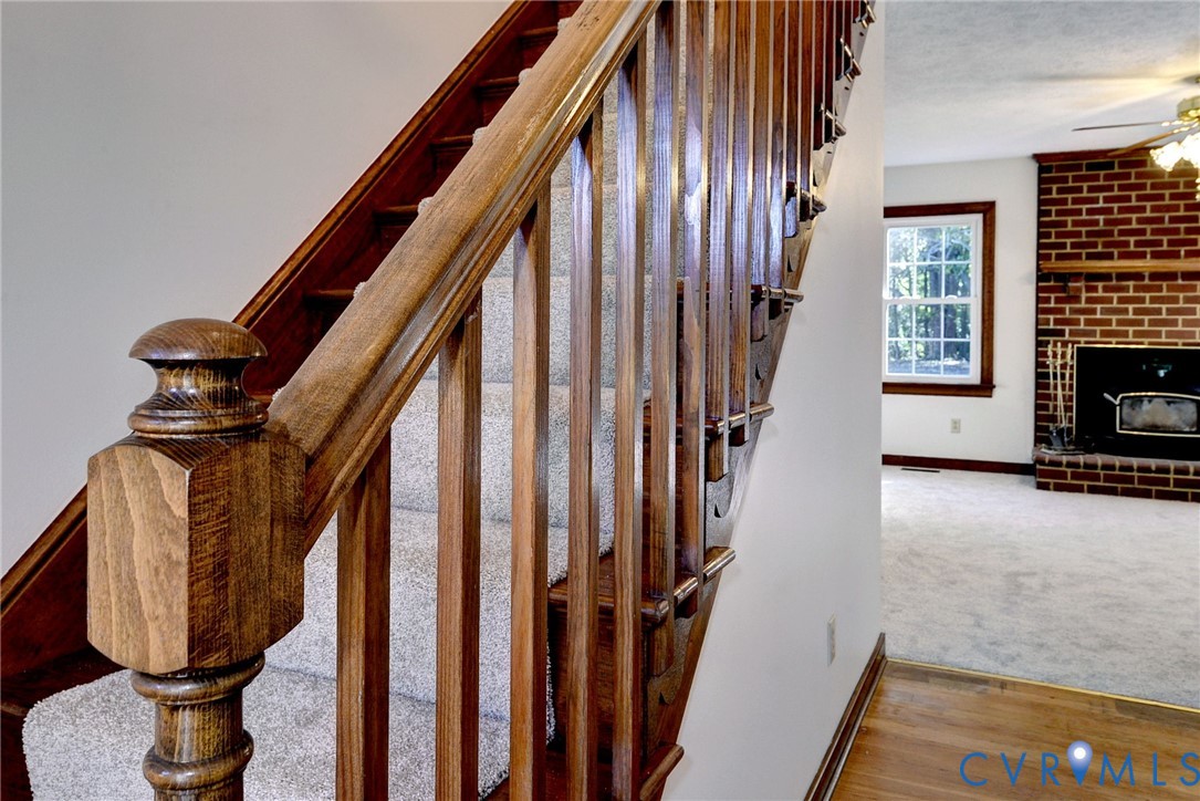 Staircase featuring stained wood balusters and a decorative newel post, with a red brick fireplace and wood-finish flooring