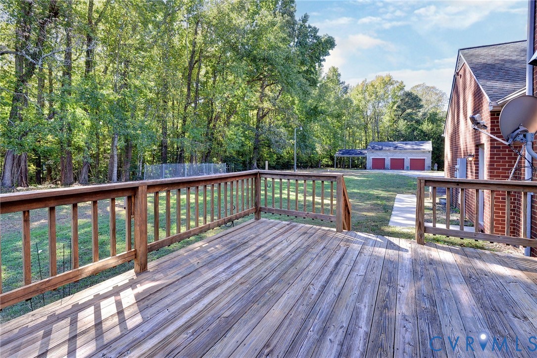 Elevated wooden deck with railings, brick exterior, sprawling grounds, mature trees, and detached three-car garage