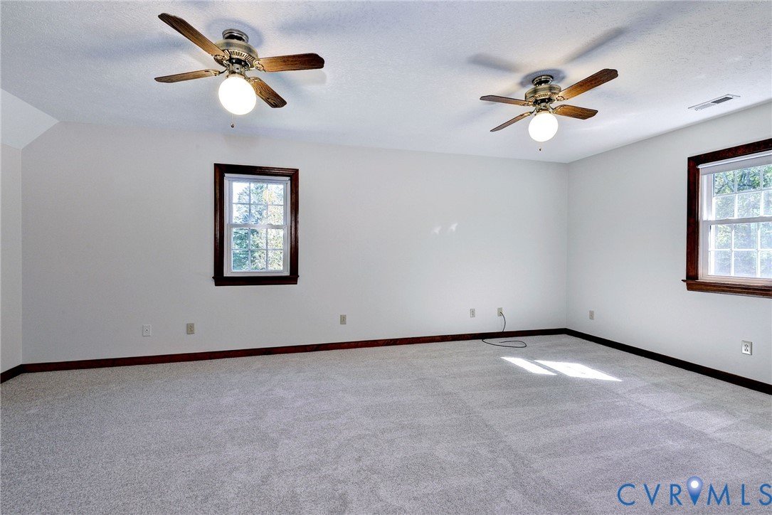 Spacious interior featuring wall-to-wall carpeting, two ceiling fans with integrated light fixtures, and dual windows finished with wood-toned trim