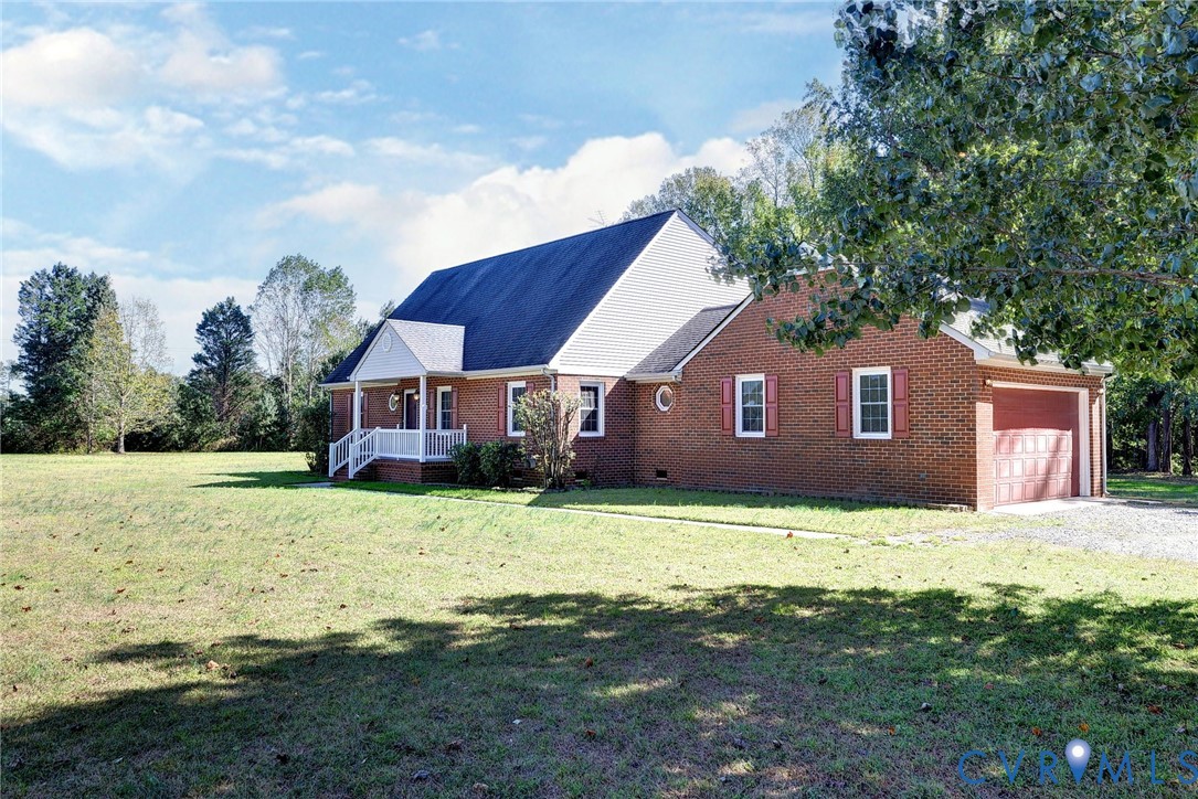 Traditional brick exterior featuring a covered front porch, attached garage, gabled roofline, and expansive grounds