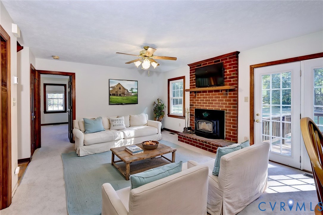 - VIRTUAL STAGING Living area featuring a floor-to-ceiling red brick fireplace, wood-cased window trim, ceiling fan with integrated lighting, and glass-paneled double doors