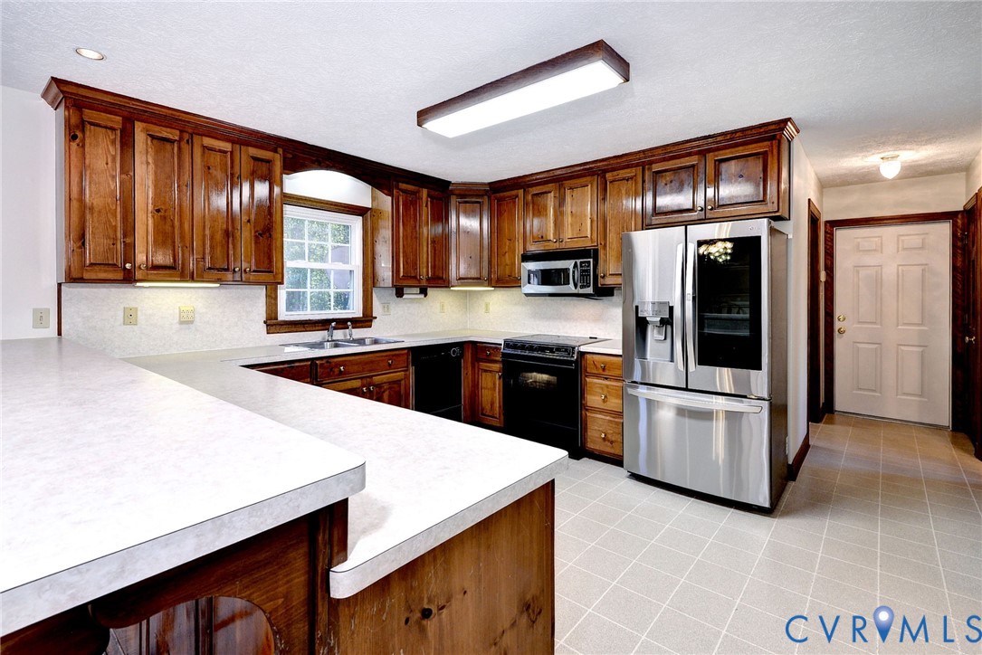 Kitchen featuring stained wood cabinetry, extended countertops, stainless steel appliances, and tiled flooring