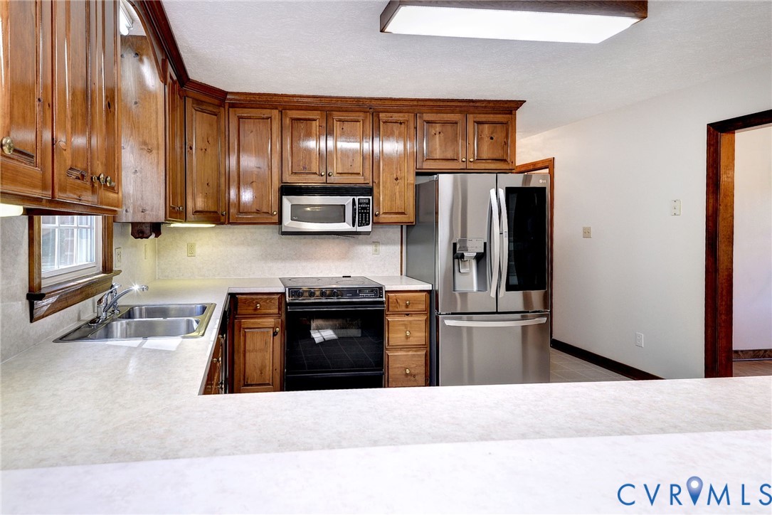 Kitchen featuring solid wood cabinetry, stainless steel refrigerator, built-in microwave, integrated electric range, and laminate countertops