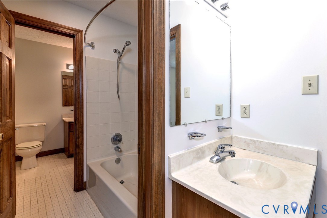 Bathroom vanity featuring a solid-surface countertop with an integrated basin, wall-mounted mirror, ceramic tile flooring, and a bathtub with a tiled surround