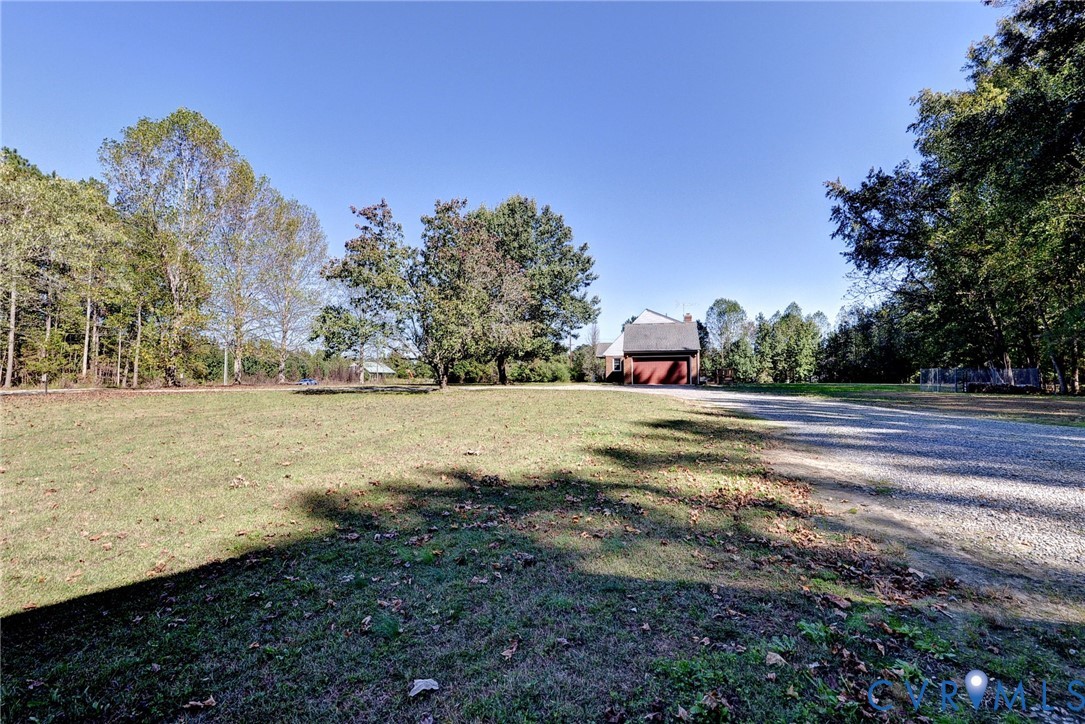 Expansive lot featuring a gravel driveway, mature trees, and a detached structure