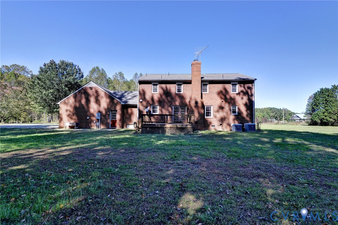 Two-story brick exterior featuring a rear wood deck, prominent masonry chimney, and expansive surrounding grounds