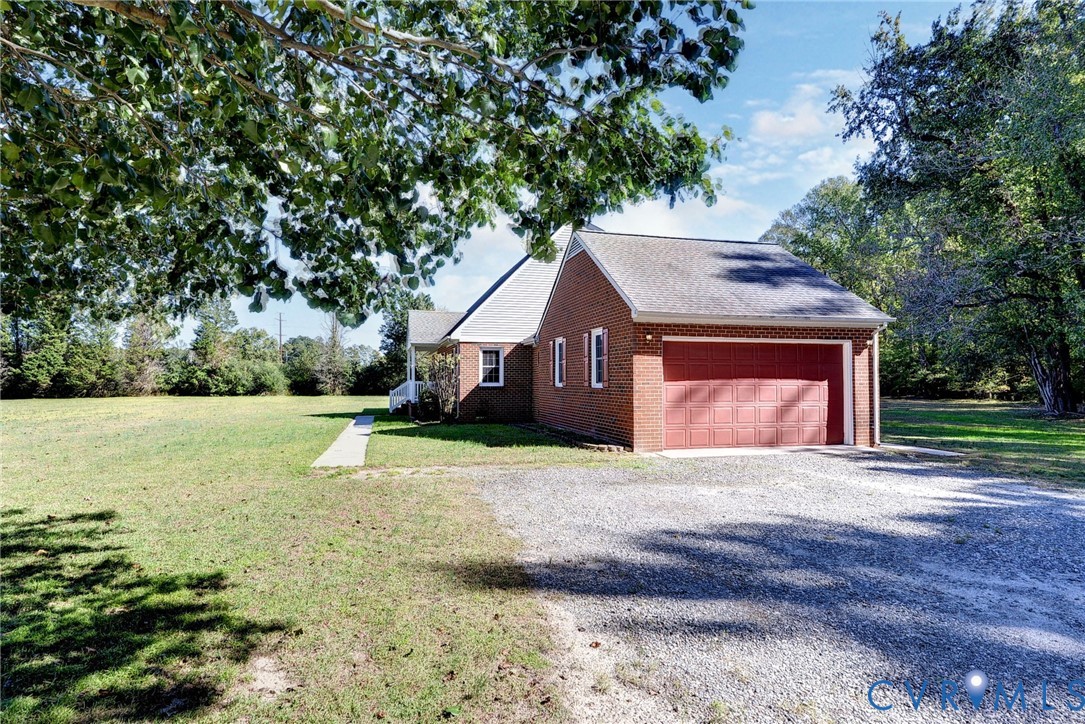 Red brick exterior featuring a multi-car garage, asphalt shingle roofing, and an expansive lawn