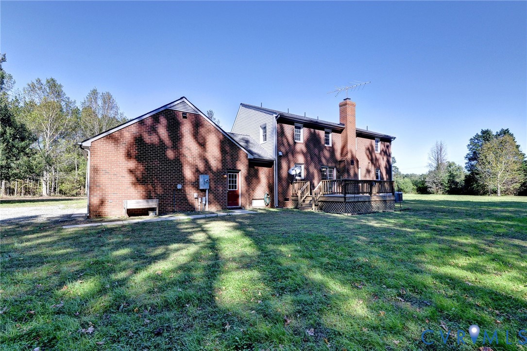 Brick exterior featuring a masonry chimney, elevated wooden deck, and expansive grass acreage