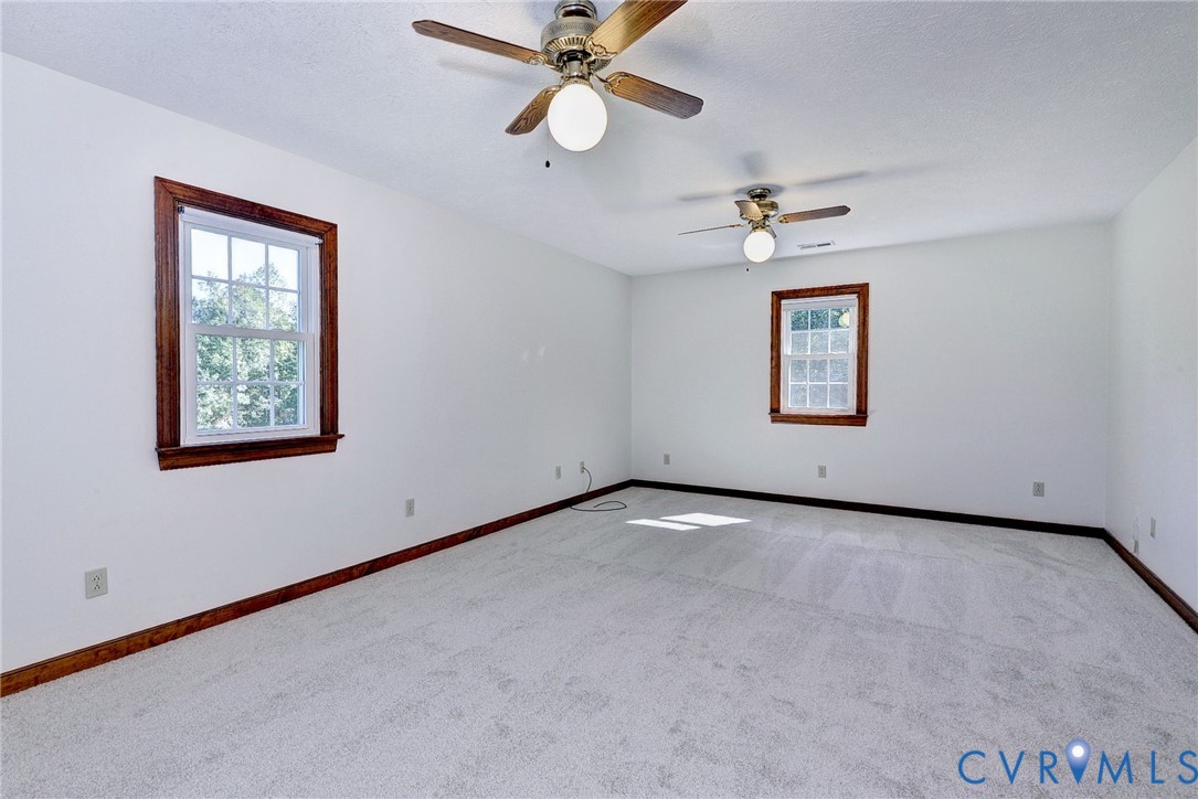 Interior space featuring wall-to-wall carpeting, dual ceiling fans with integrated lighting, and multi-pane windows framed by dark wood trim