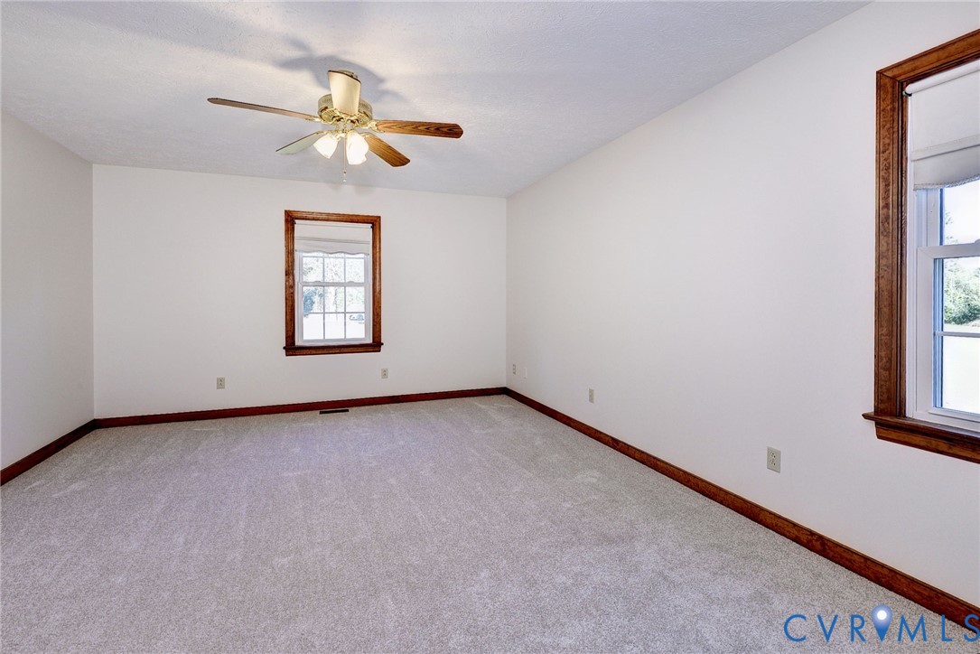 Neutral wall-to-wall carpeting, wood-trimmed window casings, and a ceiling-mounted light fixture with a multi-blade fan