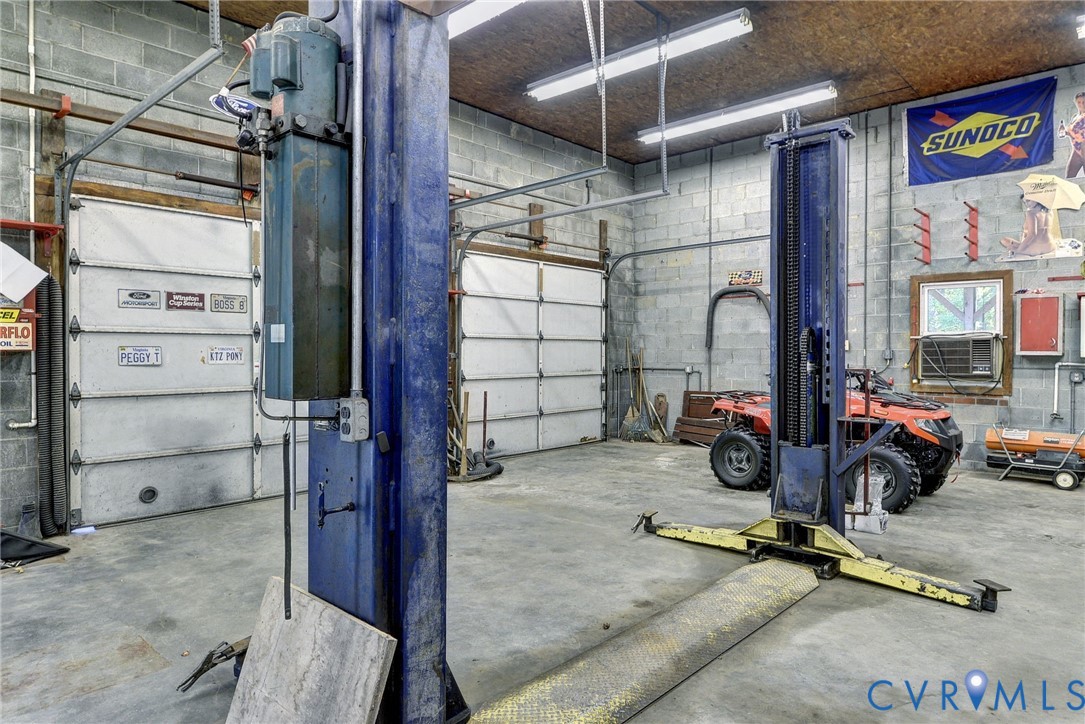 Workshop featuring concrete block walls, concrete flooring, dual metal overhead doors, and a built-in automotive lift