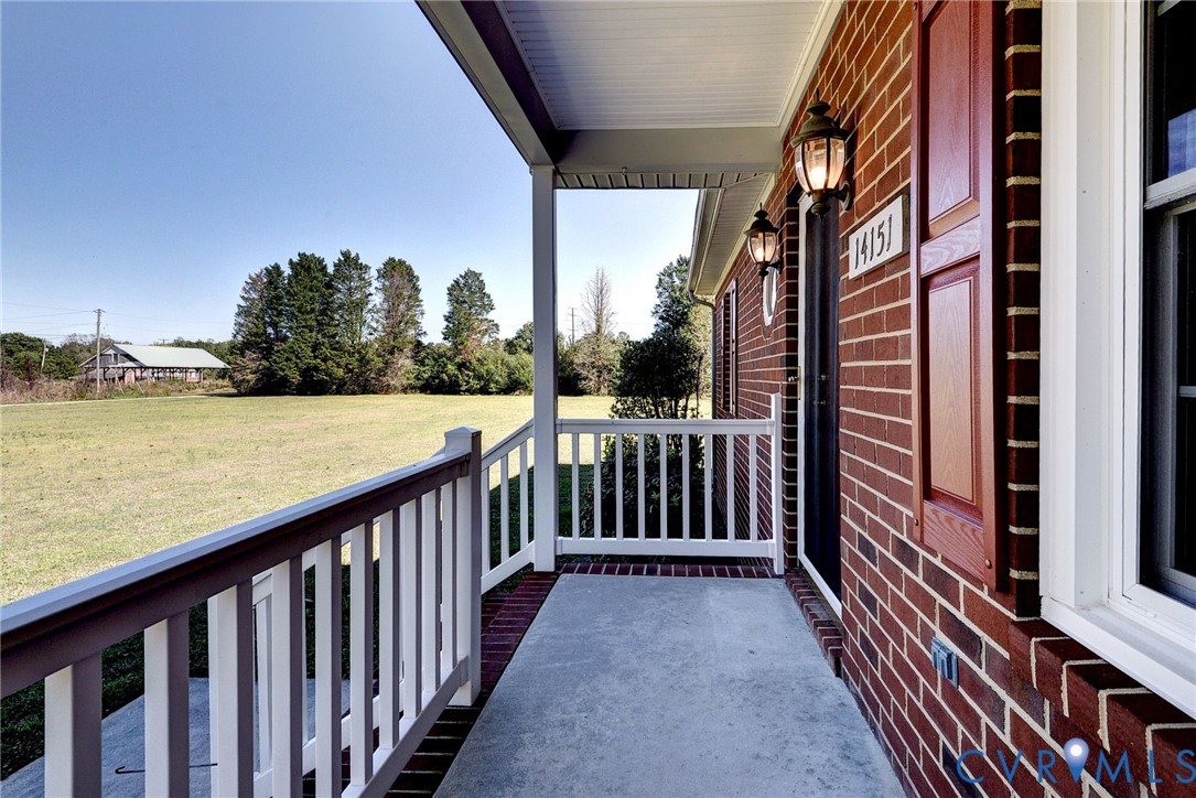 Covered front porch featuring red brick exterior, white railings, decorative shutters, and attached wall-mounted lighting