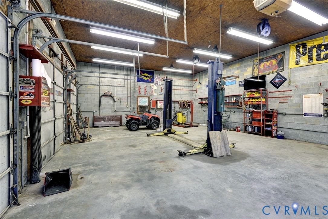 Expansive garage workspace featuring concrete block walls, concrete flooring, high-output overhead lighting, and dual vehicle lifts