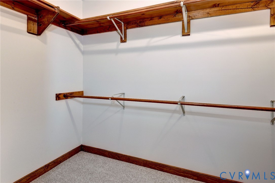 Walk-in storage space featuring wood shelving, integrated hanging rods, and neutral carpeting