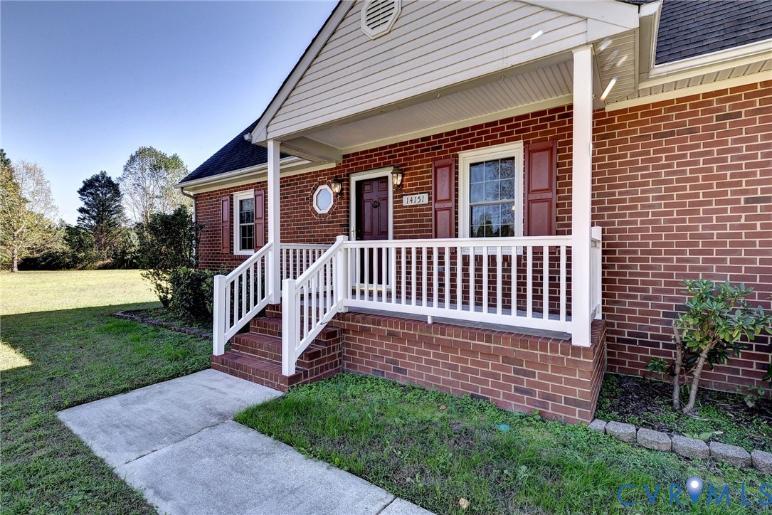 Traditional brick exterior featuring a covered front porch with white railing, vinyl siding gable, and decorative shutters