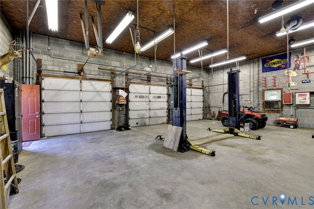 Spacious garage featuring three overhead doors, concrete flooring, exposed masonry walls, and a professional-grade automotive lift