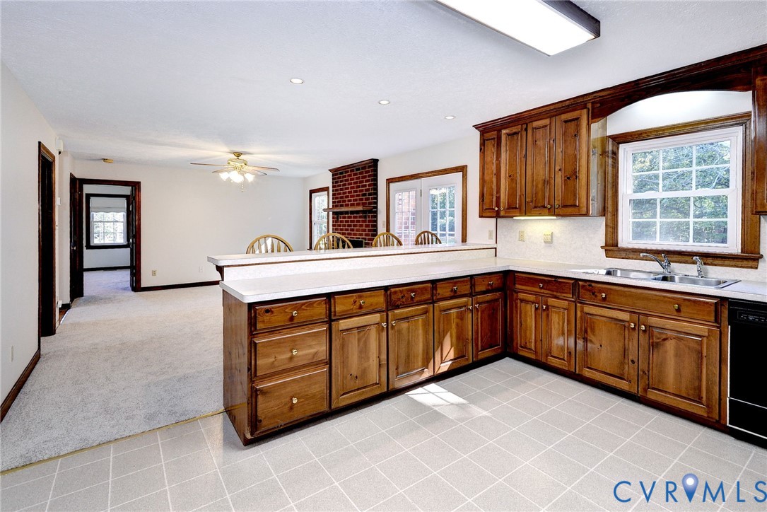 Kitchen featuring wood cabinetry, white countertops, double-basin stainless steel sink, tiled flooring, and a brick fireplace