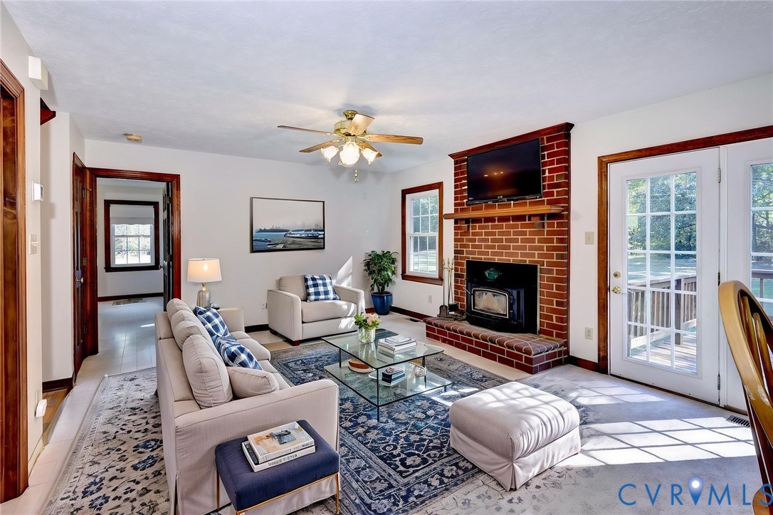 VIRTUAL STAGING - Living area featuring a floor-to-ceiling red brick fireplace, a hearth with an inset wood stove, dual glass-paned doors, and a ceiling fan with integrated lighting