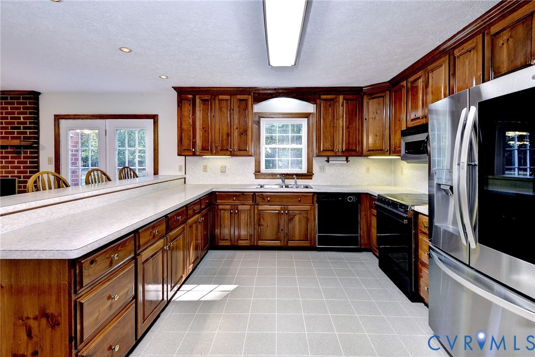 Kitchen featuring stained wood cabinetry, solid-surface countertops, tile flooring, stainless steel refrigerator, and integrated appliances