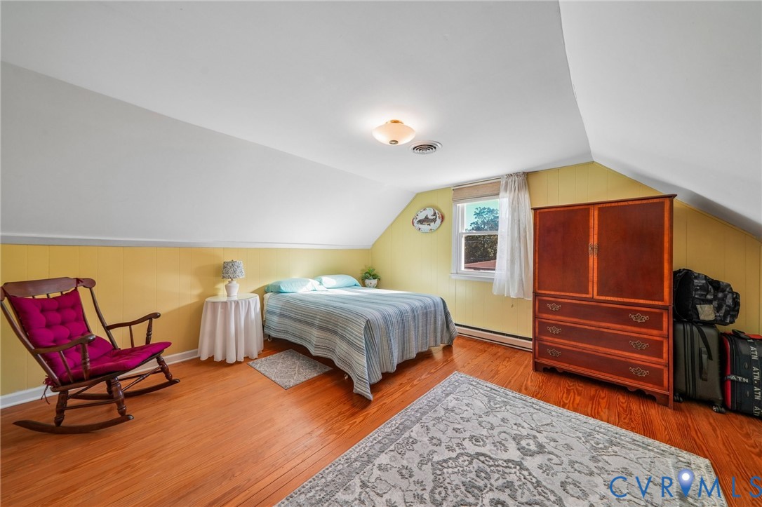 Bedroom featuring slanted ceilings, wood-finish flooring, and natural light from a single window