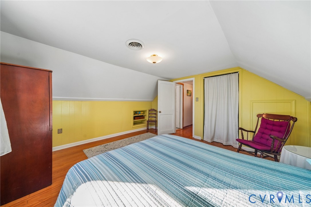 Sloped ceilings, wood-finish flooring, paneled wall detailing, and built-in shelving