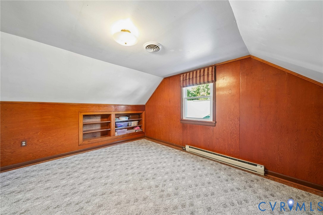Room featuring wood-panelled walls, built-in recessed shelving, patterned wall-to-wall carpeting
