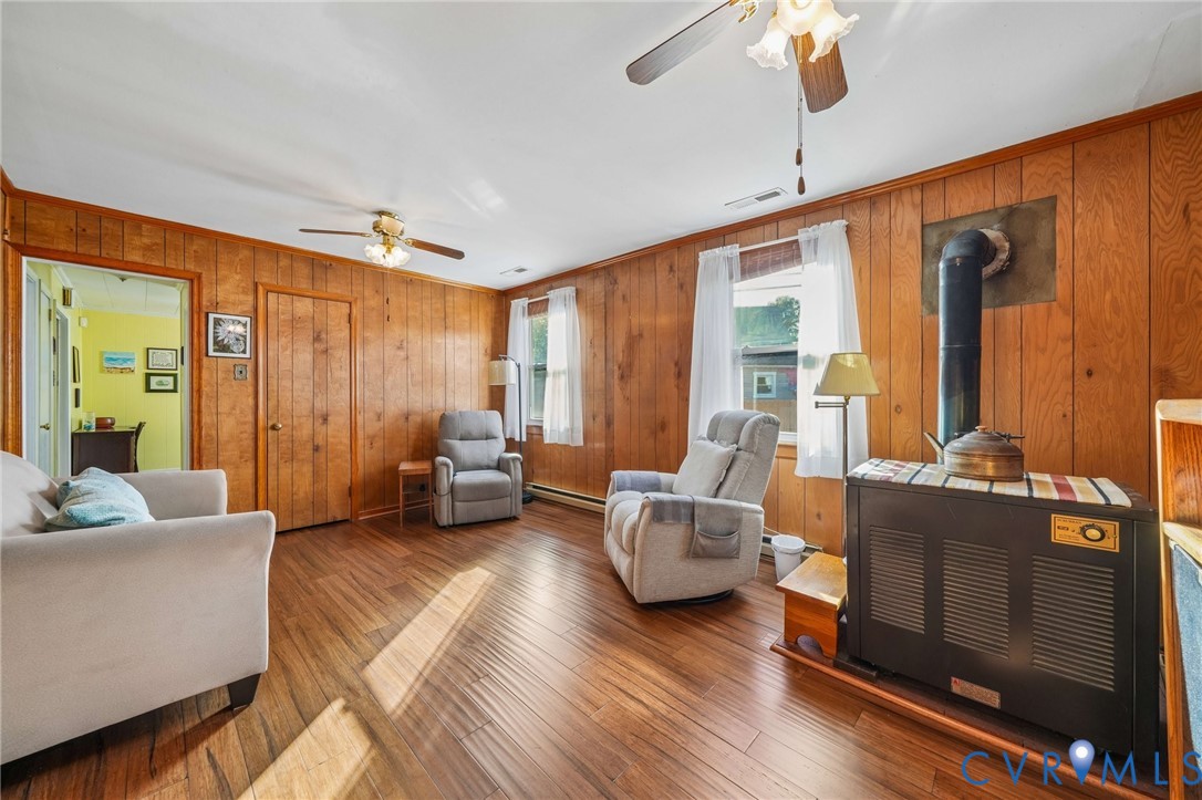 Wood-panelled interior featuring wood-finish flooring, dual ceiling fans, and a built-in metal wood heating stove Wood-panelled interior featuring wood-finish flooring, dual ceiling fans, and a built-in metal wood heating stove