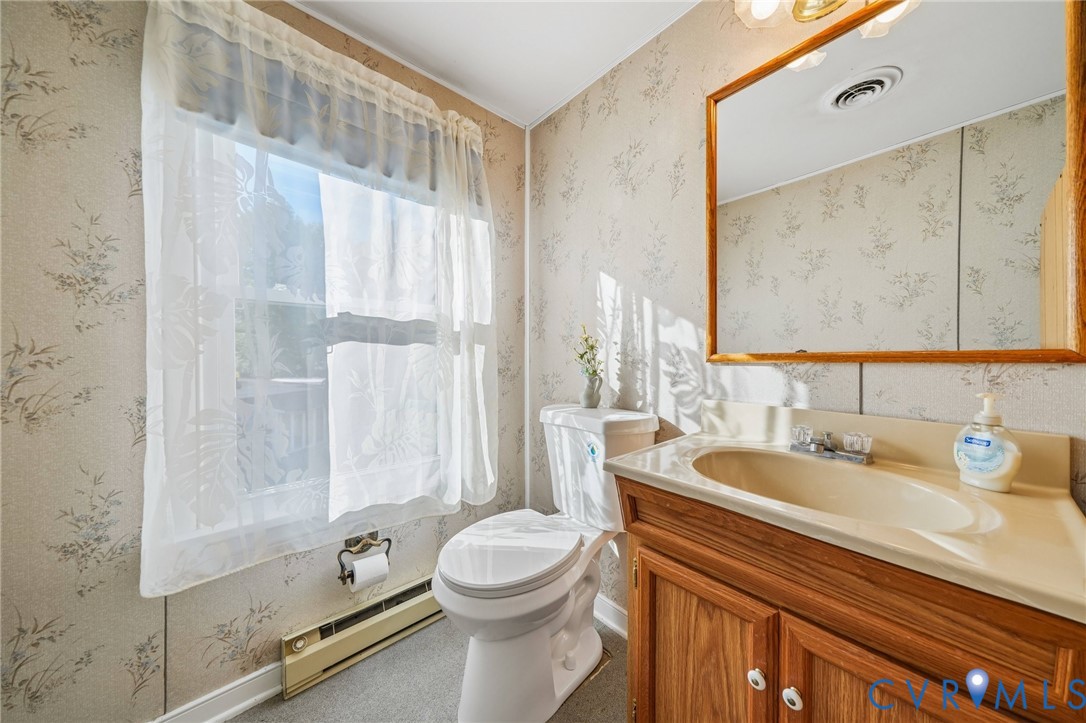 Bathroom featuring a wood-toned vanity with an integrated basin, a large framed wall mirror, patterned wallpaper, and a window with natural light