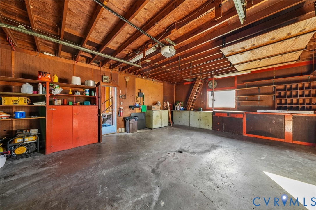 Multi-car garage featuring exposed wood ceiling joists, concrete flooring, extensive built-in storage cabinetry, open wall-mounted shelving