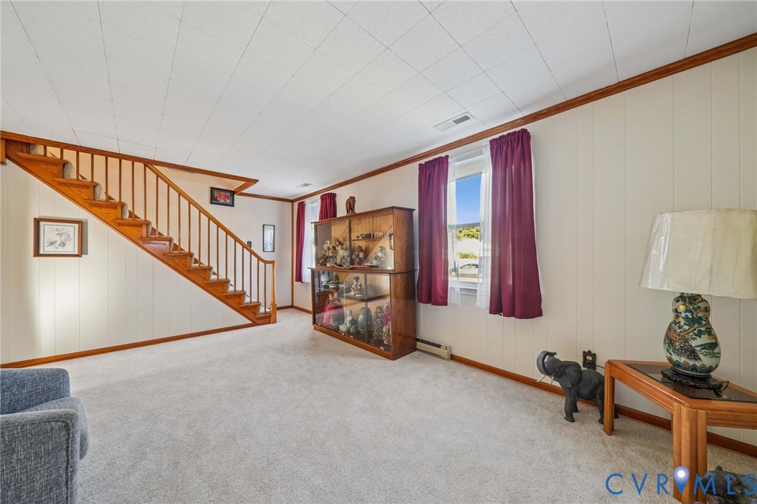 Open-concept space featuring wall-to-wall carpeting, wood-finish staircase with vertical balusters, and windows with wood-trim molding