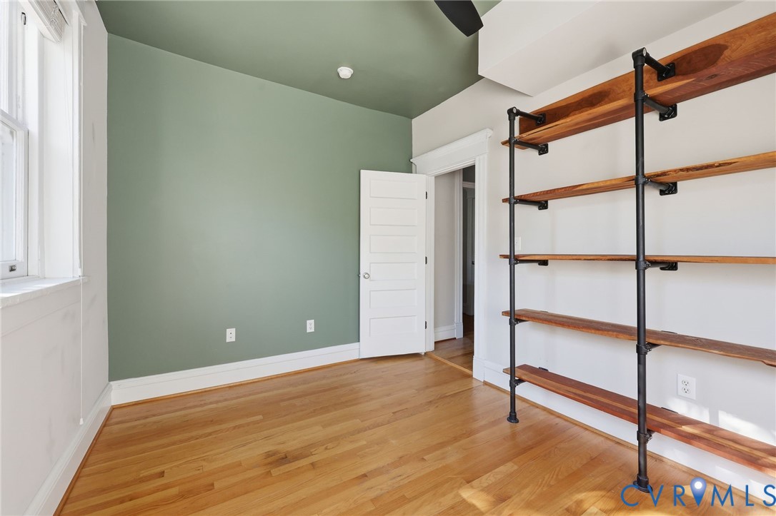 Room featuring wood flooring, industrial-style wall-mounted shelving with metal pipe supports, wood-finish shelves, and a five-panel interior door
