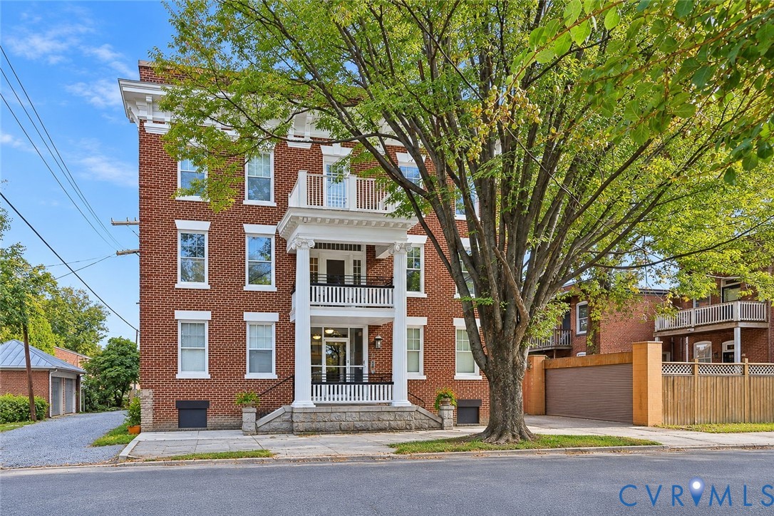Three-story brick exterior featuring a covered porch with classical columns, stacked balustraded balconies, a stone foundation, and a detached multi-bay garage