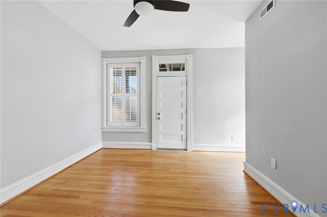 Interior room featuring wood-finish flooring, a multi-pane door with a transom window, window shutters, and a ceiling fan