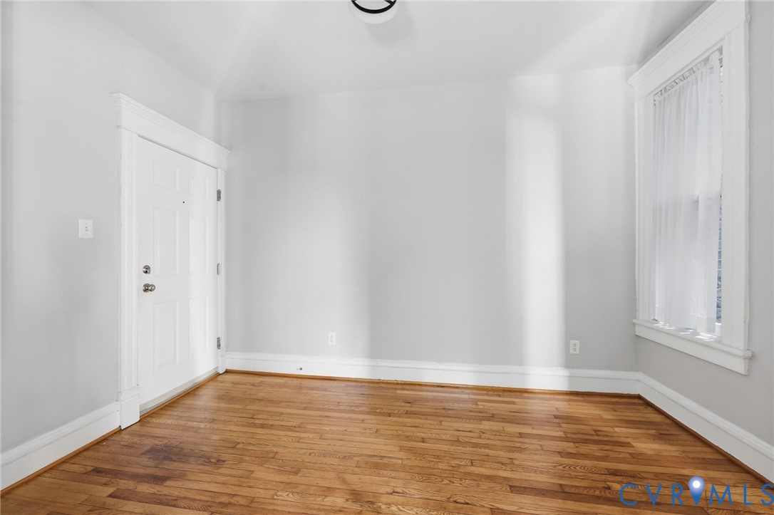 Room featuring wood-finish flooring, white multi-panel entry door, and window with white casing