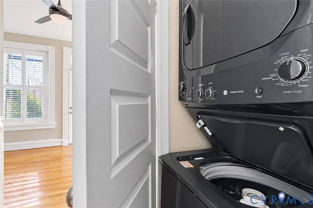 Stacked black laundry appliance with top-loading washer, wood-finish flooring, and white paneled door