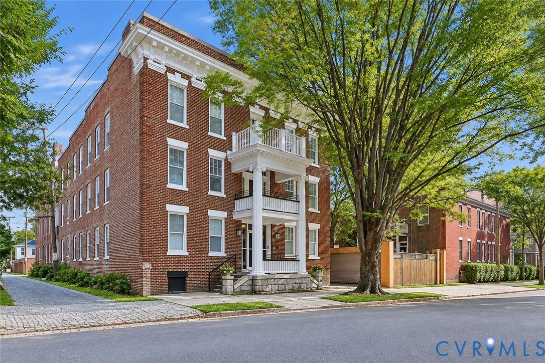 Three-story brick exterior featuring a multi-level portico with classical columns, detailed cornice work, a stone foundation, and a cobblestone driveway