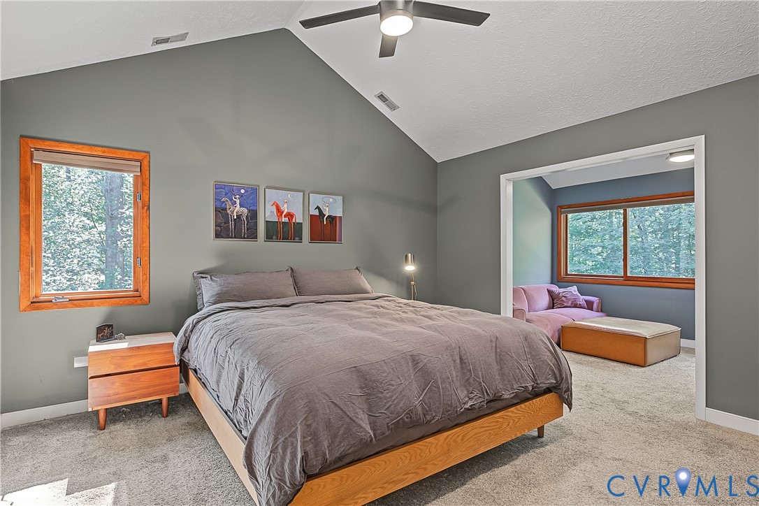 Vaulted ceiling featuring a central lighted ceiling fan, neutral wall finishes, and wood-trim windows